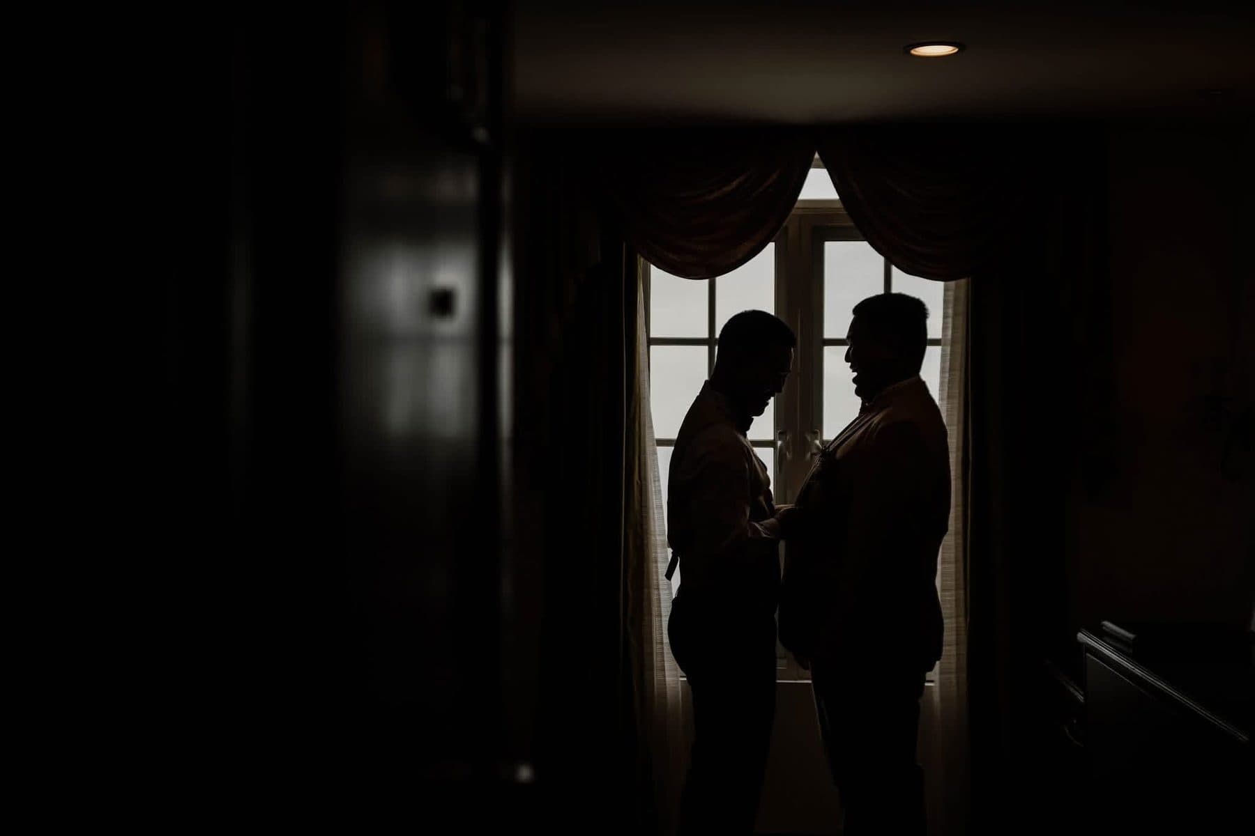 Two men getting ready by a window, in silhouette
